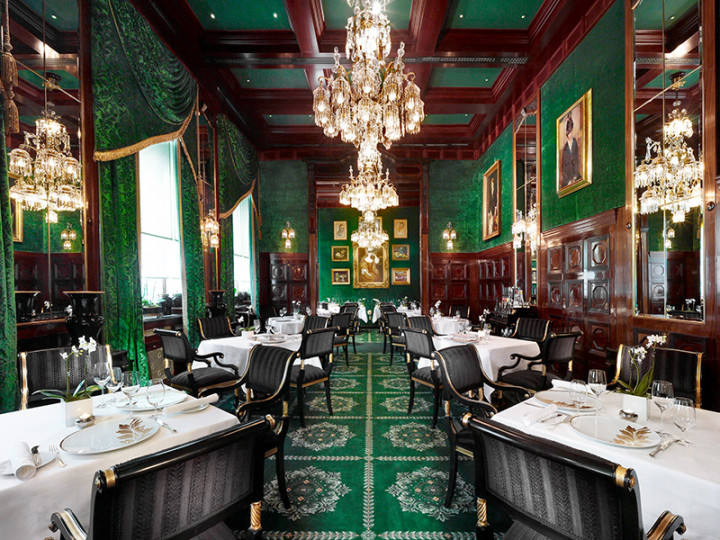 An elegant dining room with lavish interiors, emerald green décor, crystal chandeliers and classically laid tables