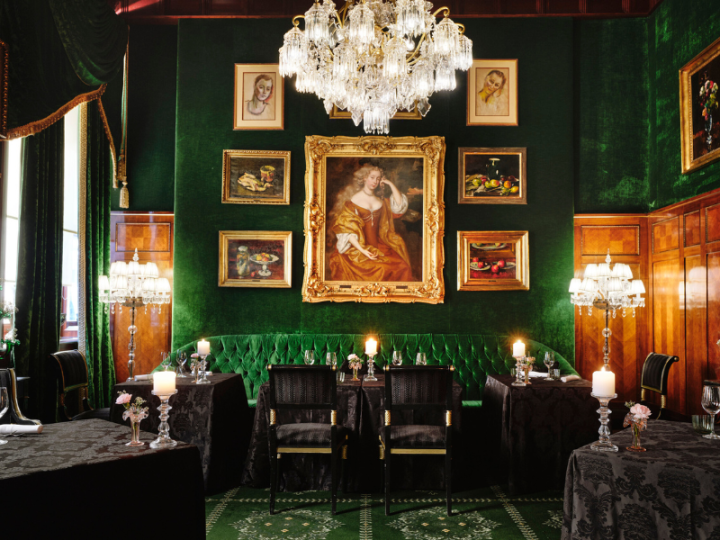 An elegant dining room with lavish interiors, emerald green décor, crystal chandeliers and classically laid tables